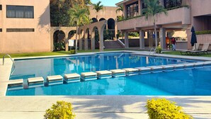 Piscina com degraus para acesso, rodeada por um edifício com varandas e céu claro.