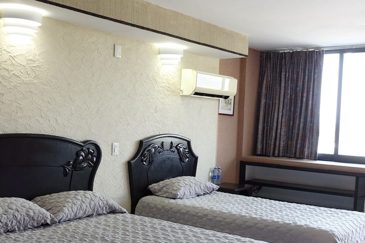 Ein Hotelzimmer mit zwei Betten, einem großen Fenster mit Vorhängen und einer Wand-Klimaanlage.