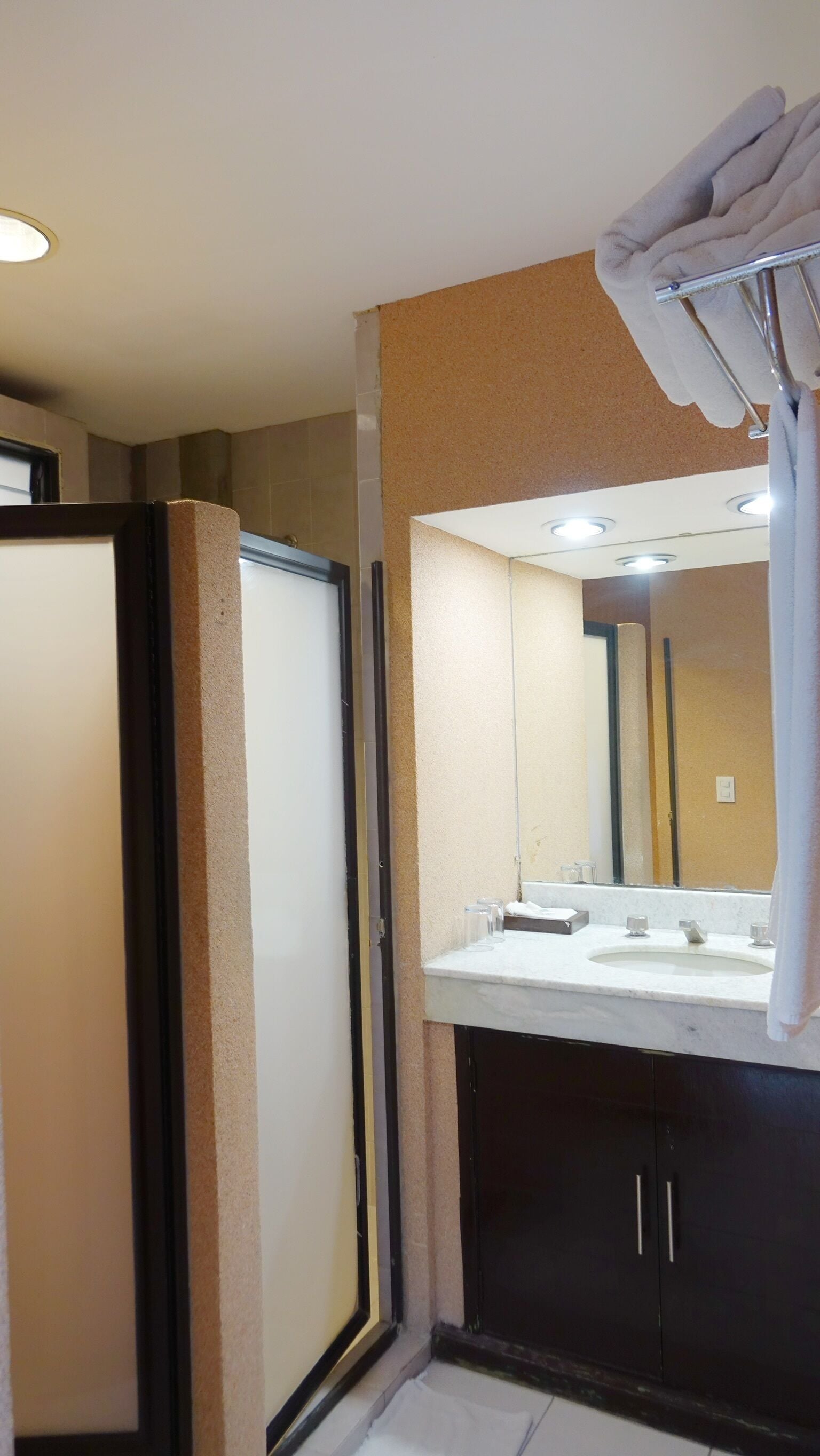 Un baño con un espejo grande, un lavabo con dos grifos y una toalla colgada en un tendedero.