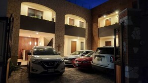 A modern building with a stone facade, multiple balconies, and a parking area with three cars. - Hotel El Descanso (Bernal)