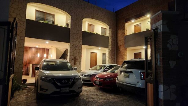 A modern building with a stone facade, multiple balconies, and a parking area with three cars. - Hotel El Descanso (Bernal)