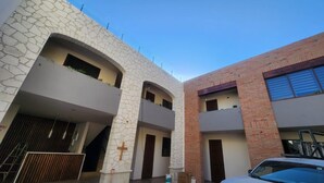 A modern building with a stone facade and a brick section, featuring balconies and a cross symbol. - Hotel El Descanso (Bernal)