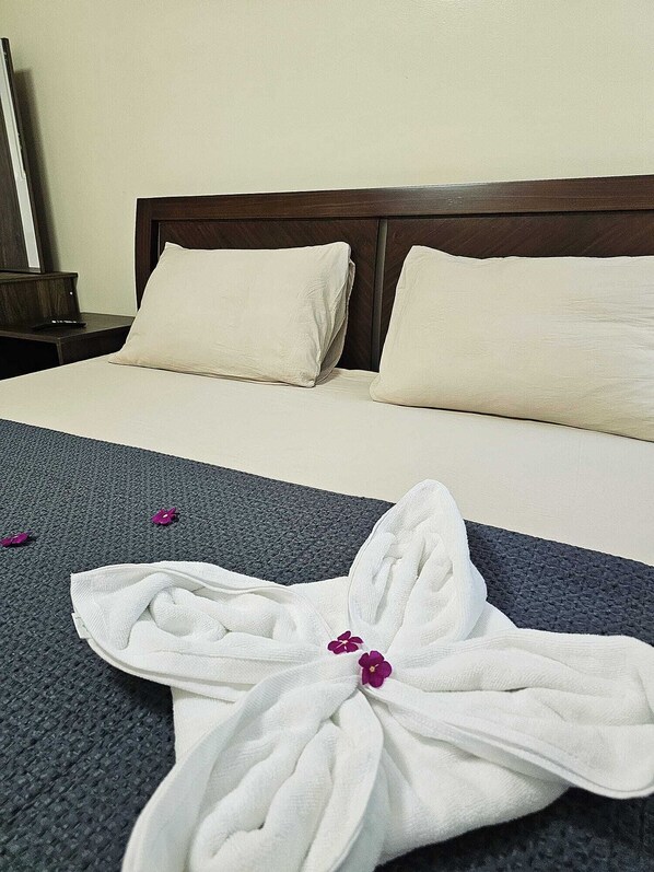 A neatly made bed with white linens, a dark headboard, and a decorative towel on the bed. - Mangotree Apartel & Resor (Panglao)