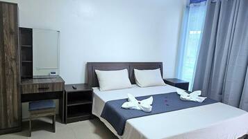 Habitación de hotel con cama, escritorio, silla, espejo y ventana con cortinas.