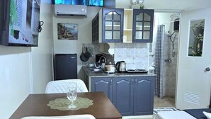 A compact hotel room with a kitchenette, a dining area with a table and chair, a bed, and a shower area. - Mangotree Apartel & Resor  (Panglao)