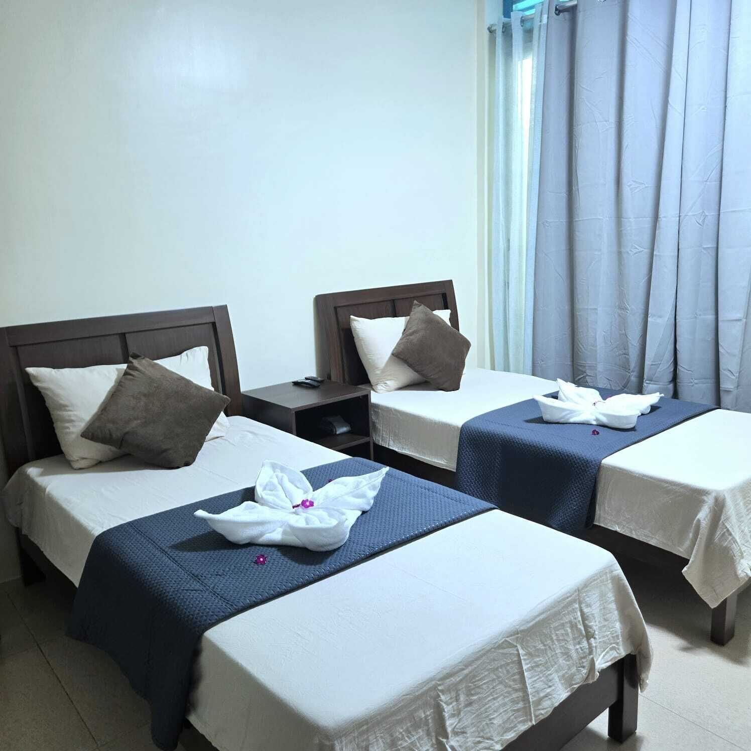 A hotel room with two beds, each with a pillow, a nightstand, and a towel on the bed.