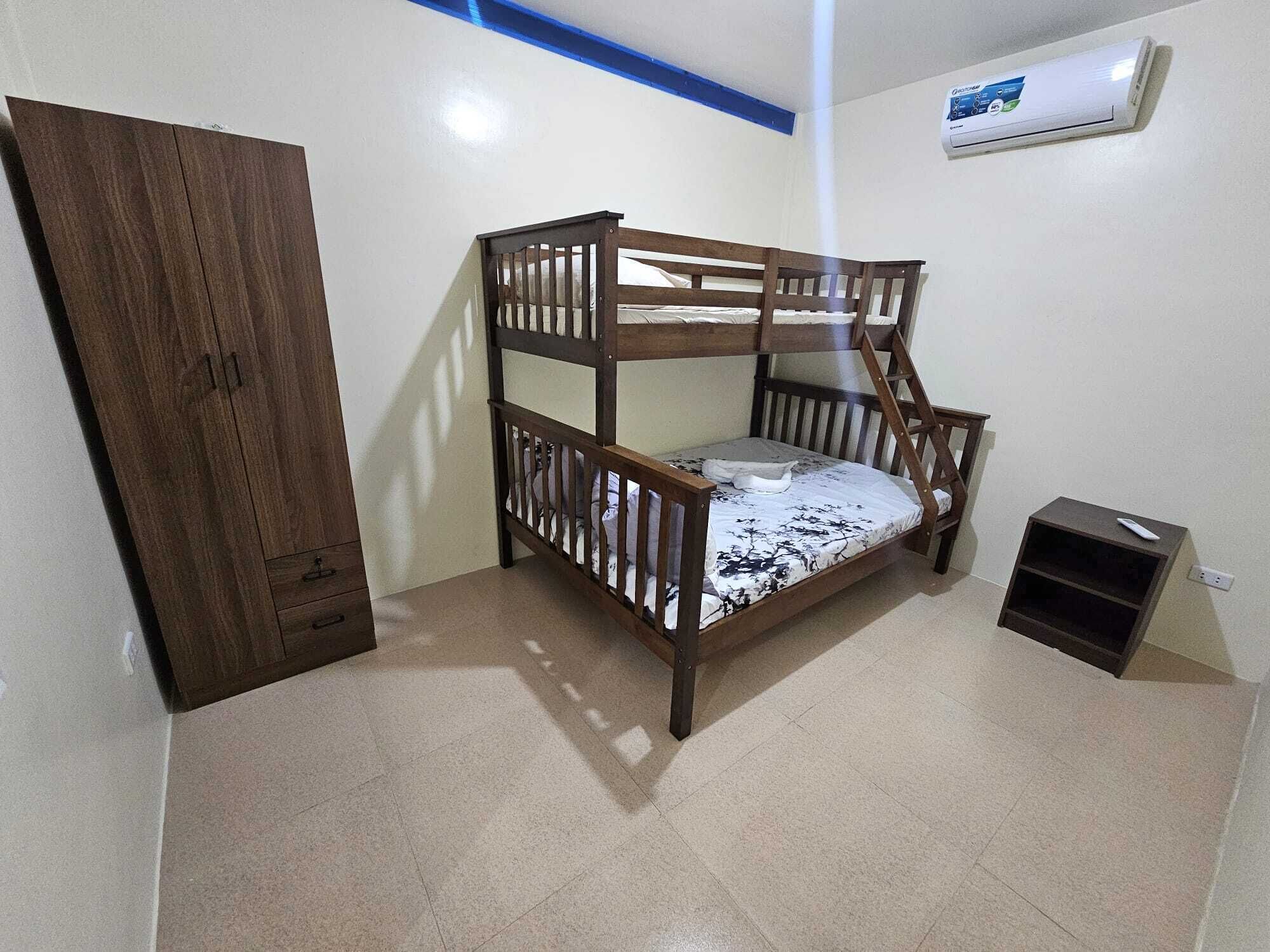 A bunk bed in a room with a wardrobe, a small shelf, and an air conditioning unit on the wall.