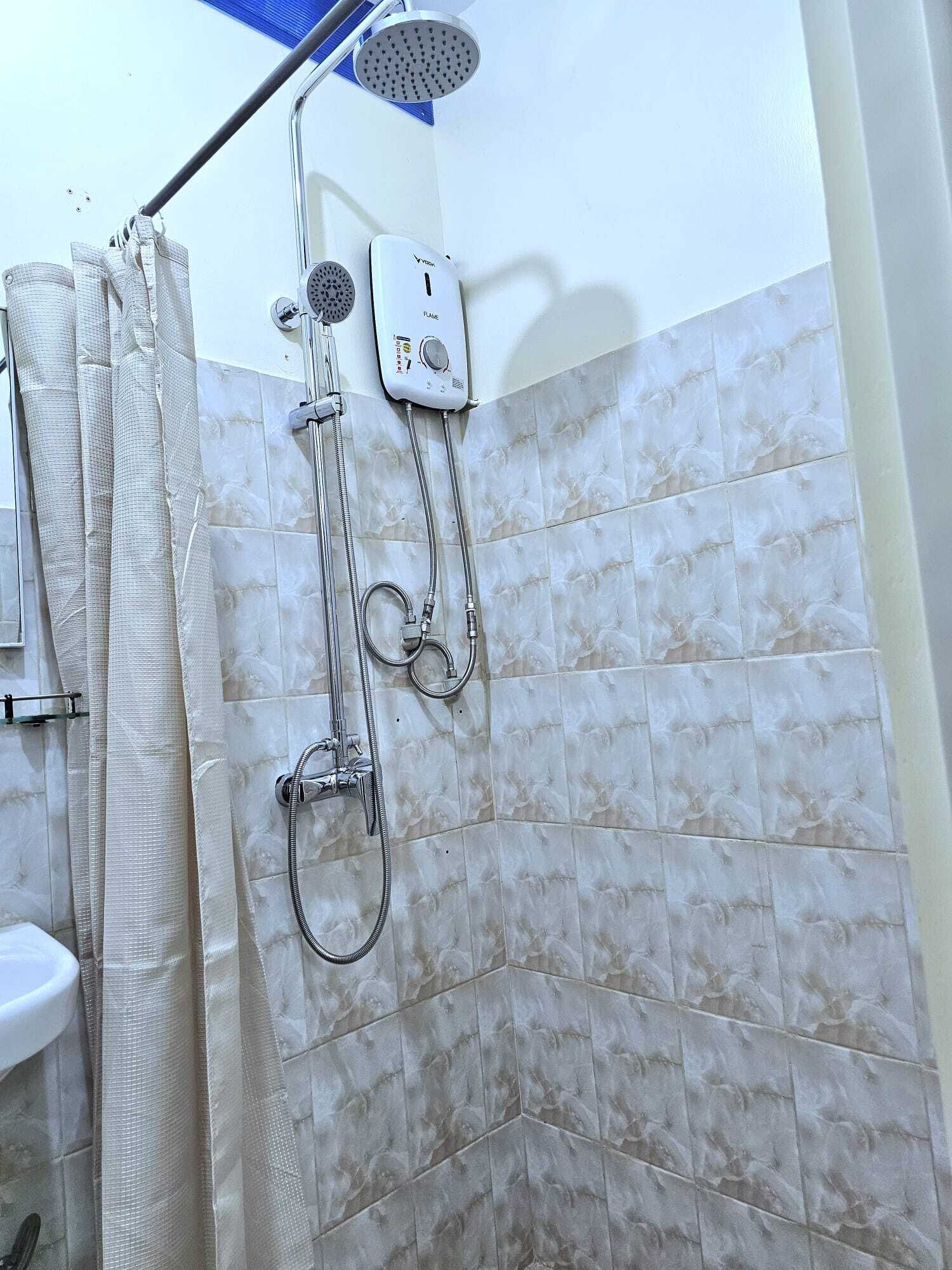 A shower with a handheld showerhead and a wall-mounted faucet, a curtain, and a tiled wall.