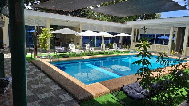A swimming pool with lounge chairs and umbrellas, surrounded by a covered patio area. - Mangotree Apartel & Resor  (Panglao)