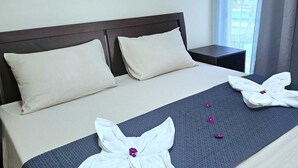 A neatly made bed with two pillows, a dark blue textured blanket, and two towels folded into flower shapes with purple flowers. - Mangotree Apartel & Resor  (Panglao)