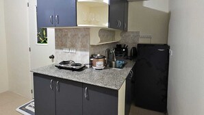 A compact kitchen with dark cabinets, a granite countertop, a built-in oven, and a small refrigerator. - Mangotree Apartel & Resor  (Panglao)