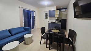 A compact living space with a blue sofa, a dining table with chairs, a small round table, and a kitchen area with cabinets and a refrigerator. - Mangotree Apartel & Resor  (Panglao)
