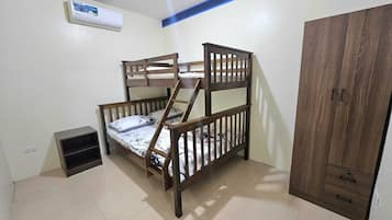 A bunk bed with a wooden frame and a small shelf below it, a wardrobe with two drawers, and an air conditioning unit on the wall.