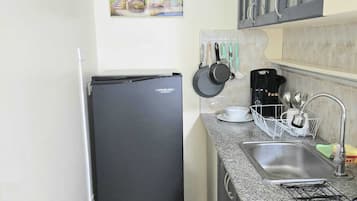 A compact kitchen with a black refrigerator, a granite countertop, a sink with a faucet, and a hanging pot rack.