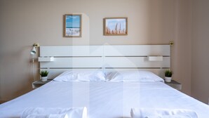 Ein ordentlich gemachtes Bett mit weißen Bettwäsche und zwei aufgerollten Handtüchern, eine Nachttischlampe und zwei kleine Blumentöpfe auf den Nachttischen.