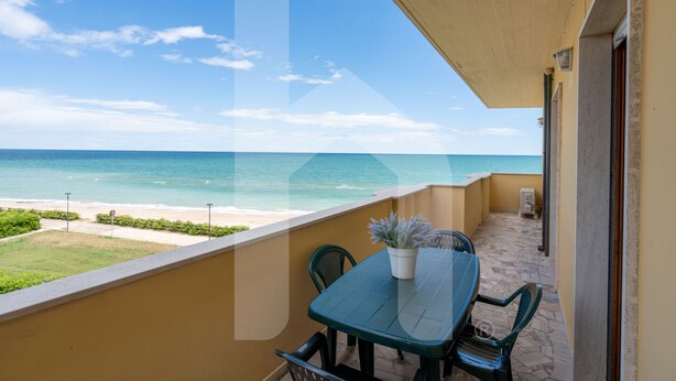 Ein Balkon mit Tisch und Stühlen, der Blick auf einen Strand und den Ozean bietet.
