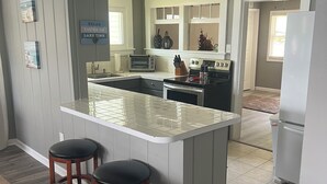 Een moderne keuken met een centraal eiland, barstoelen, een koelkast en uitzicht op de woonkamer.