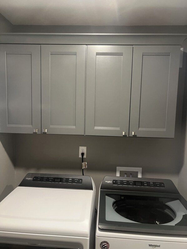 A laundry room with two Whirlpool washers and dryers, grey cabinets above, and a power outlet on the wall. - Charming 2-bedroom cottage with AC, WiFi on Pleasant Lake (Pleasant Lake)