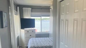 Een slaapkamer met een bed, een dressoir, een televisie en uitzicht op het water.