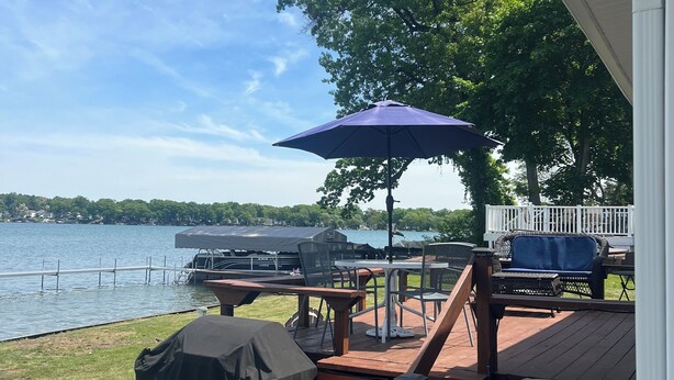 Een terras met buitenmeubilair, een overdekte barbecue en uitzicht op een meer.