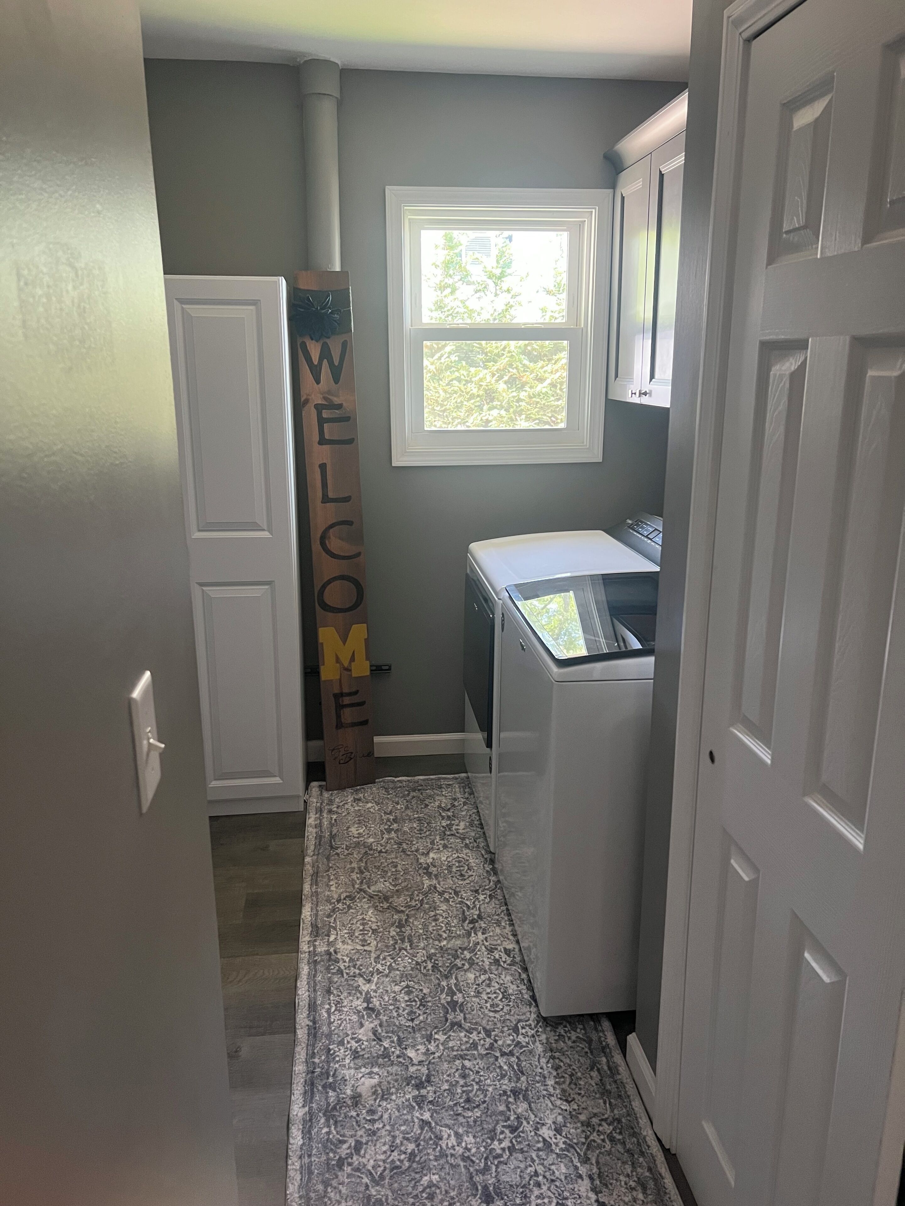 A laundry room with a washing machine, a dryer, and a window with a view of greenery.