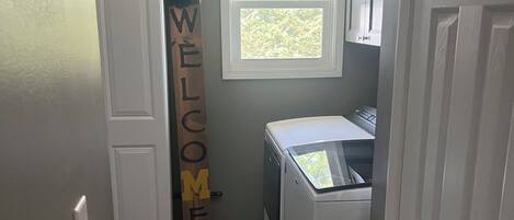 A laundry room with a washing machine, a dryer, and a window with a view of greenery.