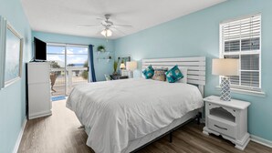 A bedroom with a bed, bedside tables, a ceiling fan, a window with blinds, and a view of the outdoors.