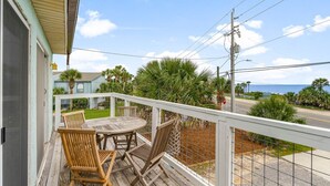 A wooden deck with a table and chairs, overlooking a road and palm trees.