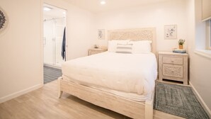 Une chambre à coucher comprenant un lit, des tables de chevet, une commode, une fenêtre et une porte donnant sur une salle de bain.