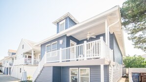 Un immeuble résidentiel à deux étages, doté d’un balcon, d’un porche et d’un escalier apparent menant à l’étage supérieur.