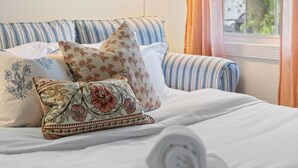 Un lit bien fait, avec une literie à rayures et des coussins à motifs floraux, une lampe suspendue et des tableaux encadrés accrochés au mur.