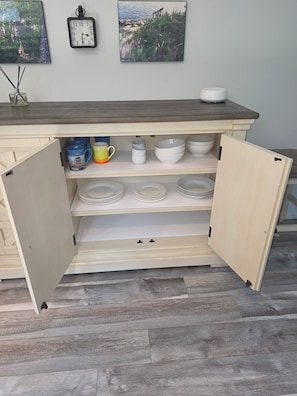 A kitchen with open cabinets revealing dishes and a clock on the wall. - Round Pond Maine - Charming apartment for 4 with AC, WiFi and ocean view. (Round Pond)