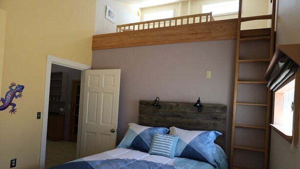 Een slaapkamer met een stapelbed, een houten hoofdbord, een ladder en een deur naar een andere kamer.