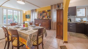 A dining area with a table set for four, a kitchen with dark cabinets, and a window with curtains.
