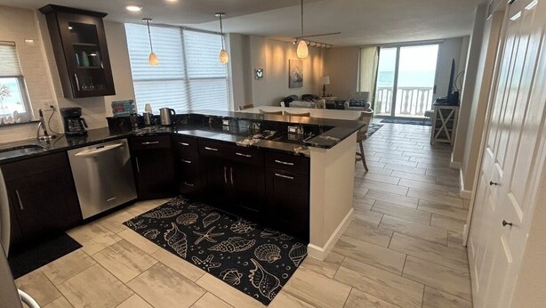 A modern kitchen with dark cabinetry, a central island, and a dining area with a view.