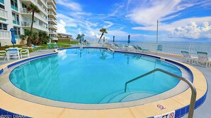 A pool area with a view of the ocean, surrounded by lounge chairs and a building with balconies.