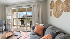 Un salon moderne avec un canapé gris, une table basse en bois et un balcon offrant une vue sur les immeubles.