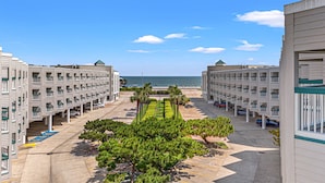 Un hôtel situé en bord de mer, composé de bâtiments à plusieurs étages, doté d’une cour centrale agrémentée d’arbustes soigneusement taillés et offrant une vue sur l’océan.