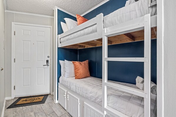 Habitación con literas, una puerta blanca, felpudo y pared azul.