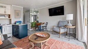 Une cuisine moderne avec un îlot central bleu, un coin repas avec une table en bois et un salon avec un canapé et un téléviseur.