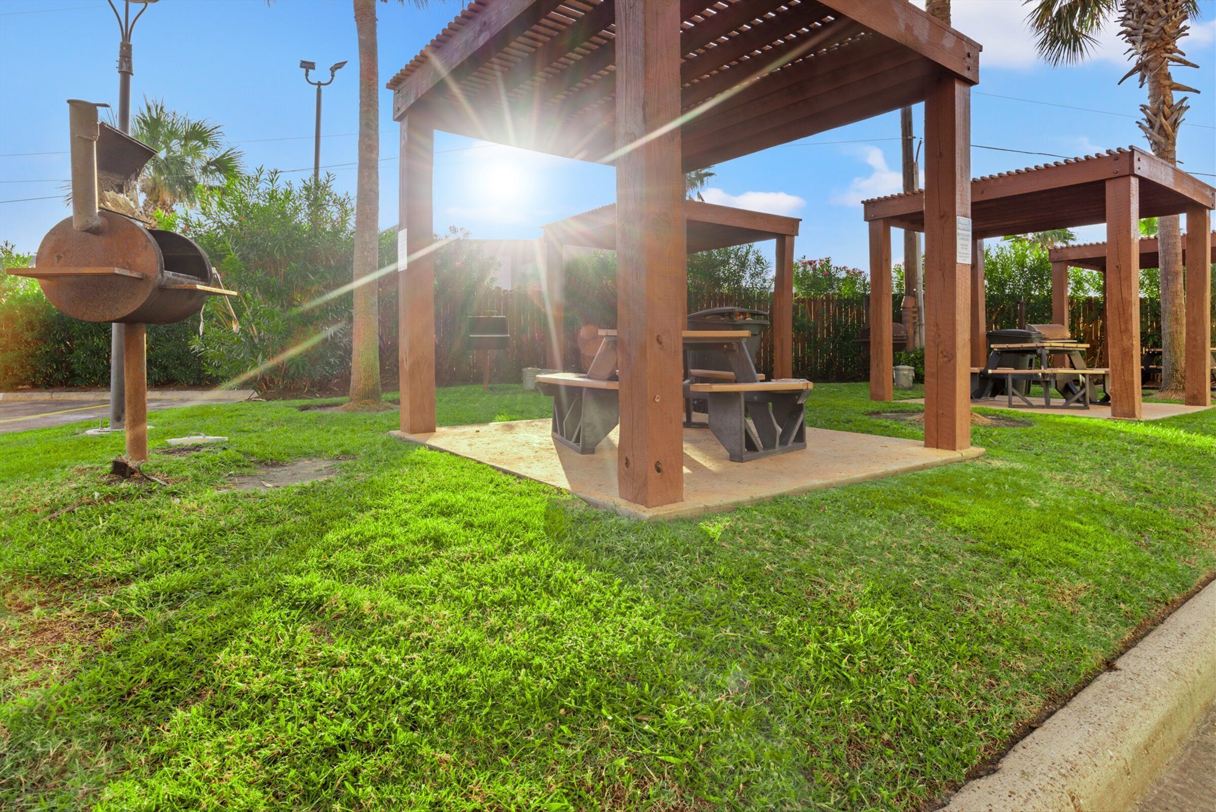 A gazebo with a grill and seating area, surrounded by well-maintained grass and palm trees.