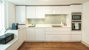 A modern kitchen with white cabinets, a stainless steel sink, a coffee maker, a microwave, and two ovens.