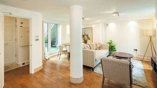 A modern living room with a wooden floor, a white sofa, a dining table, and a large column.