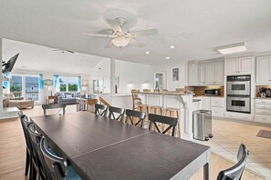 A spacious kitchen with white cabinets, a dining area with a large table and chairs, and a ceiling fan.