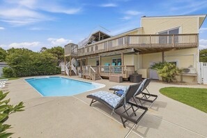 A two-story house with a swimming pool, outdoor furniture, and a covered deck.
