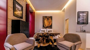 Une chambre d’hôtel moderne avec un grand lit, deux fauteuils, une table basse en bois et un tapis noir à poils longs.