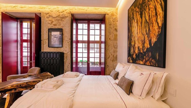 Une chambre d’hôtel avec un grand lit, une table de chevet en bois, une porte rouge et un grand tableau accroché au mur.