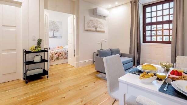 Una sala de estar moderna con comedor, un sofá gris, una mesa de centro blanca y un ventanal con cortinas.