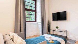 Una habitación de hotel con una cama, un sofá, un televisor montado en la pared y una pequeña mesa con una planta.