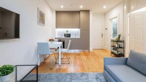 Una sala de estar moderna con un sofá gris, una mesa de comedor con sillas y una zona de cocina con armarios y una encimera.